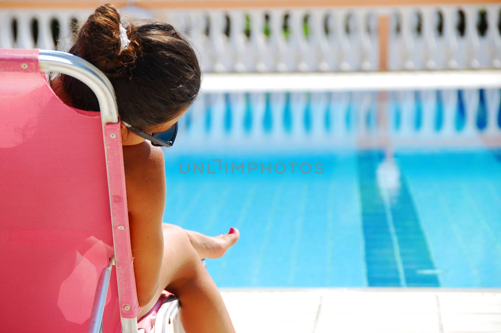 teenage girl sitting by the blue clear transparent swimming pool