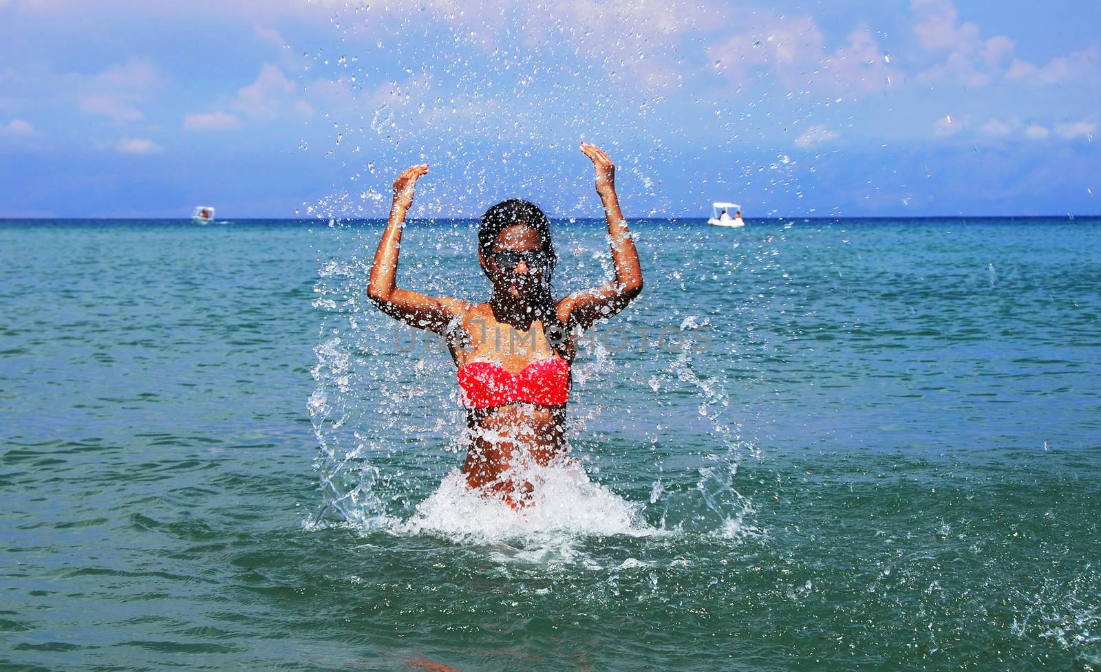 slim caucasian teenage girl with raised hands splashing water in the blue Ionic sea, Greece