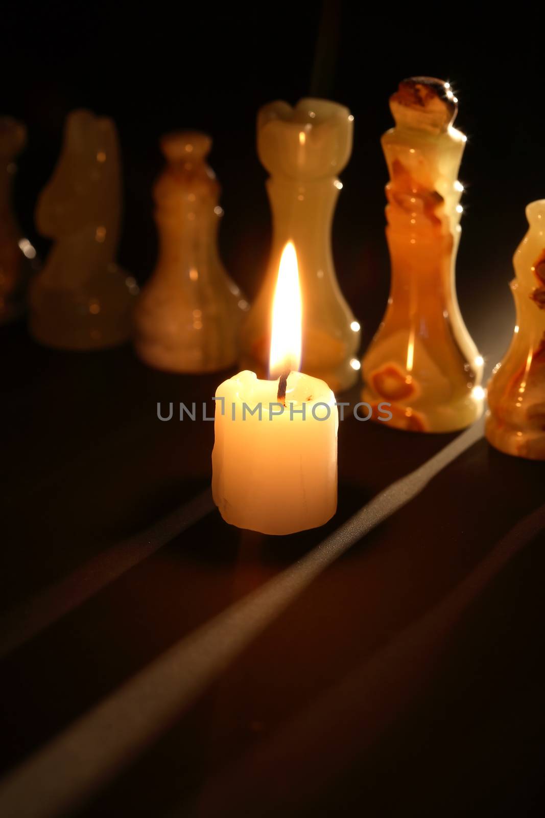 Set of chess pieces made from onyx against lighting candle on dark background