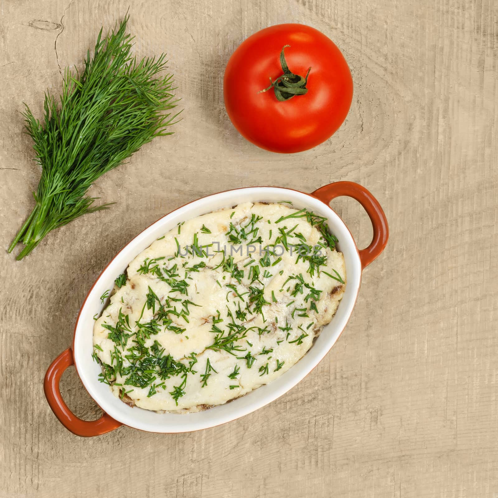 Julienne mushrooms baked in cream sauce, in a bowl for baking on a wooden background. Bunch of dill and tomato, place for text.