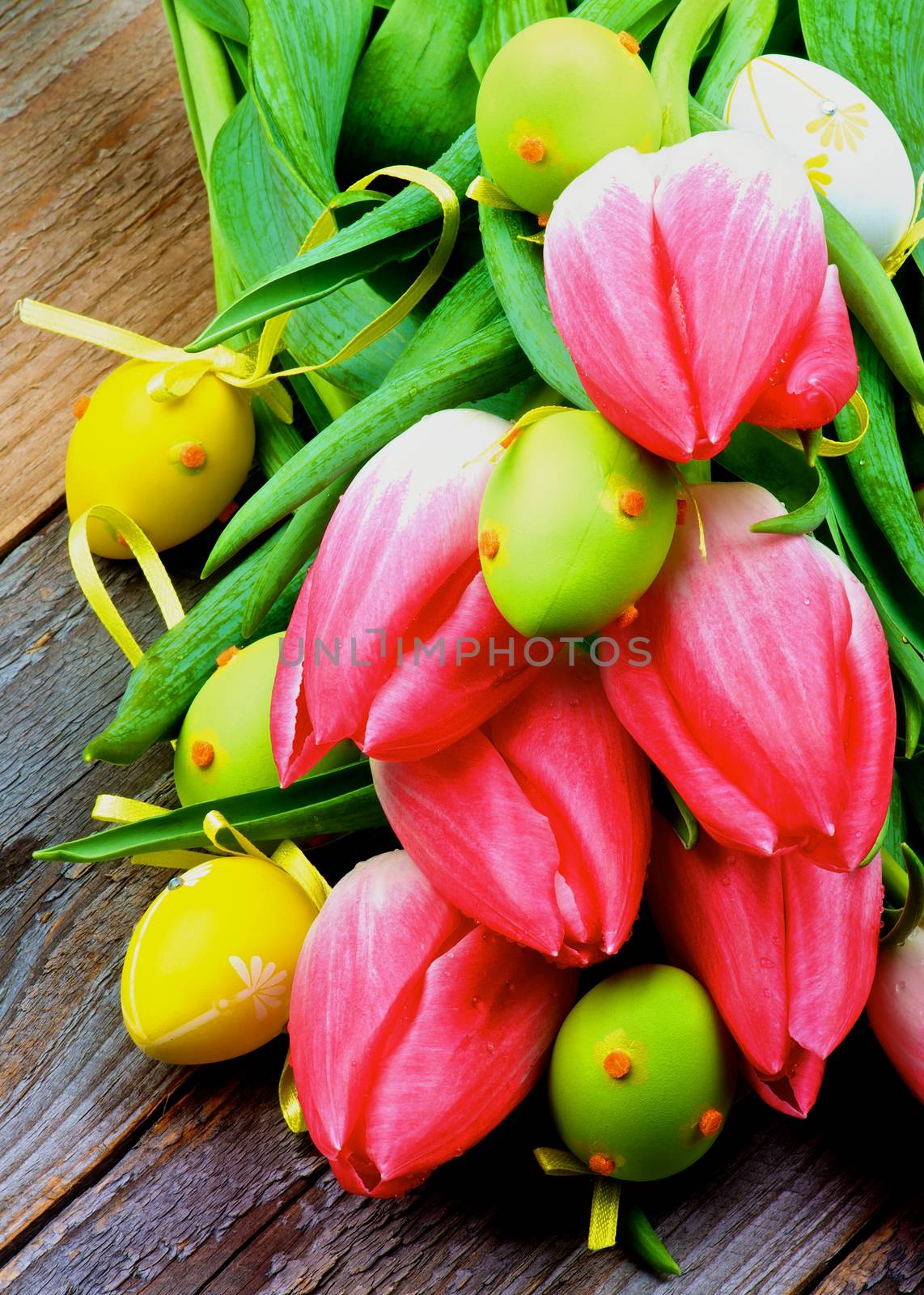 Colorful Easter Theme with Bunch of Magenta Tulips and Yellow and Green Spotted Easter Eggs closeup on Rustic Wooden background
