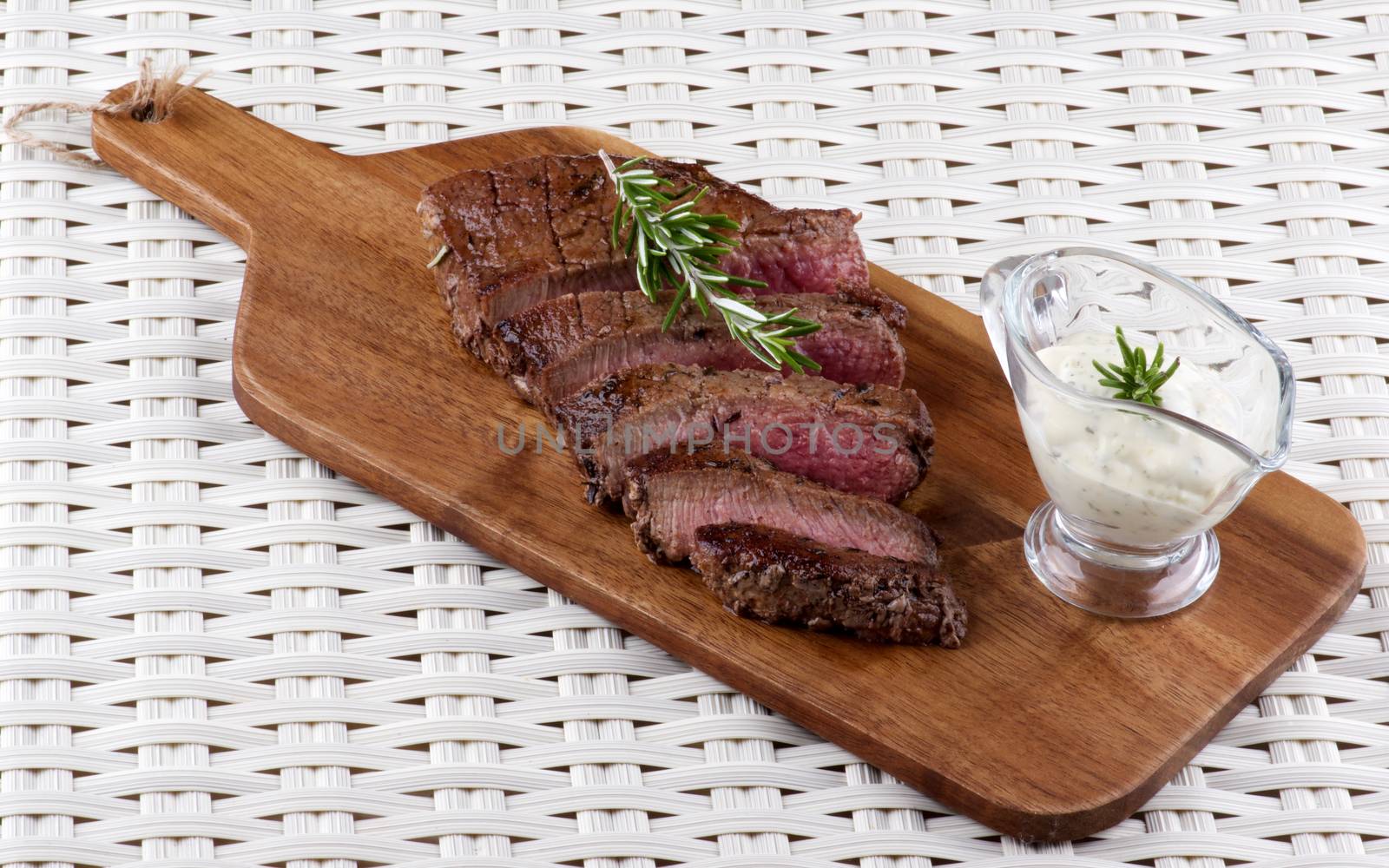 Delicious Roast Beef Medium Rare Sliced on Wooden Cutting Board with Blue Cheese Sauce and Rosemary on Wicker background