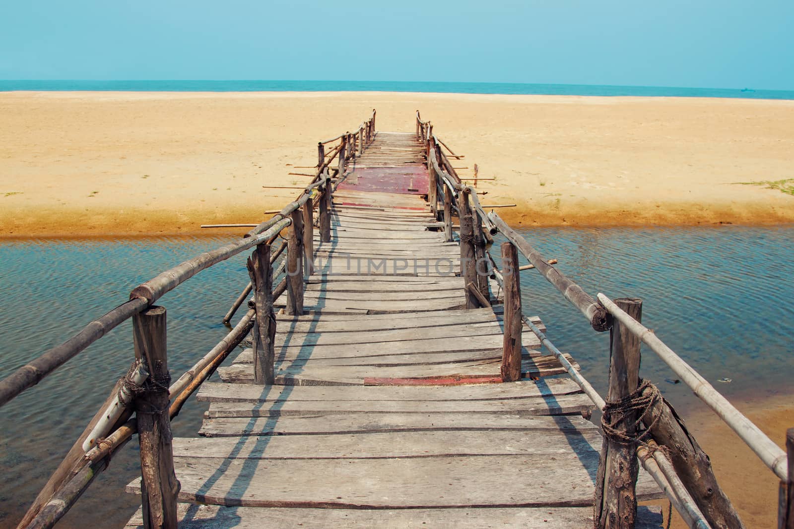Creative travel photo with blue sky, sea, beach and wood plank road leading far away