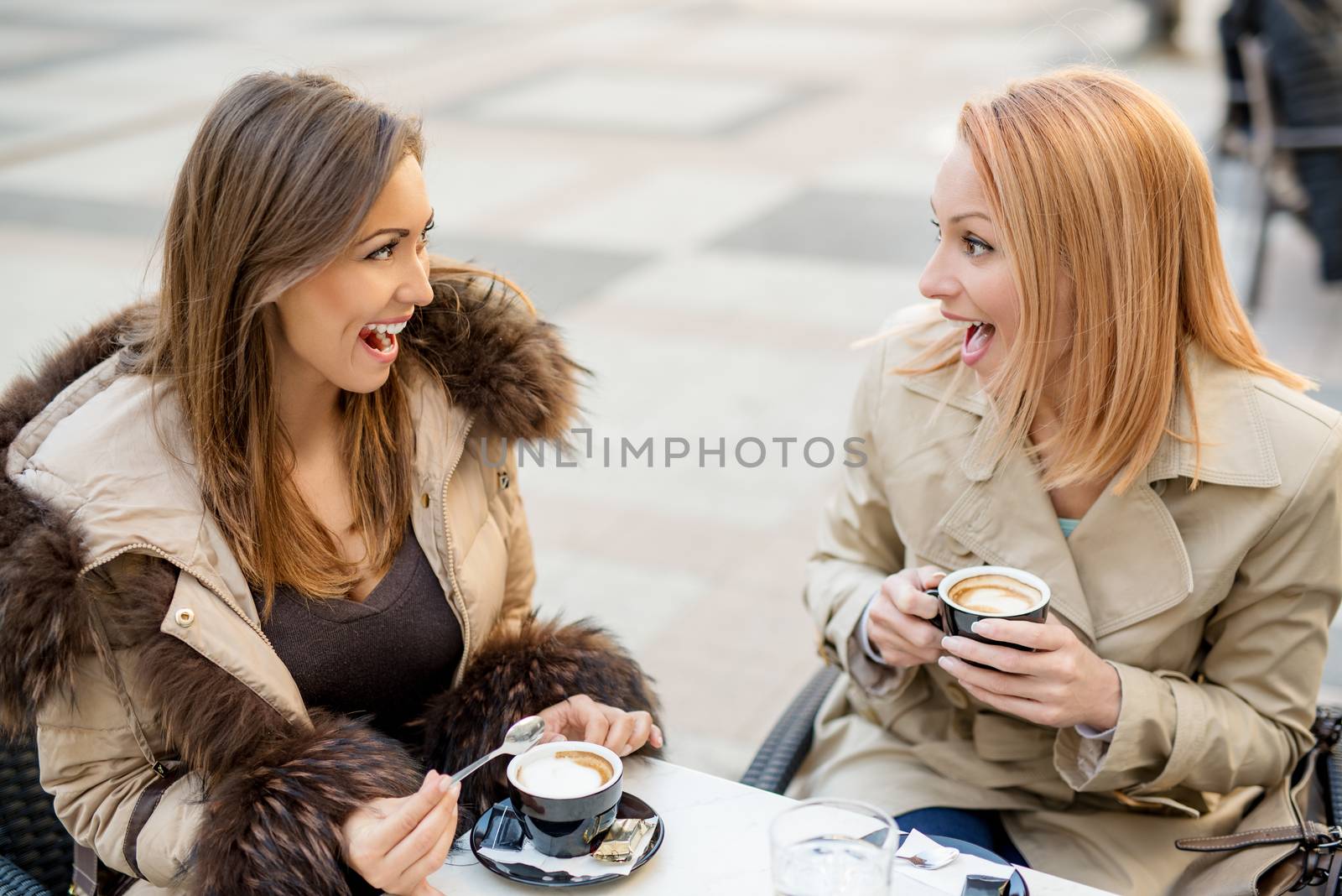 Young cheerful female friends sitting in a street cafe and enjoying coffee.