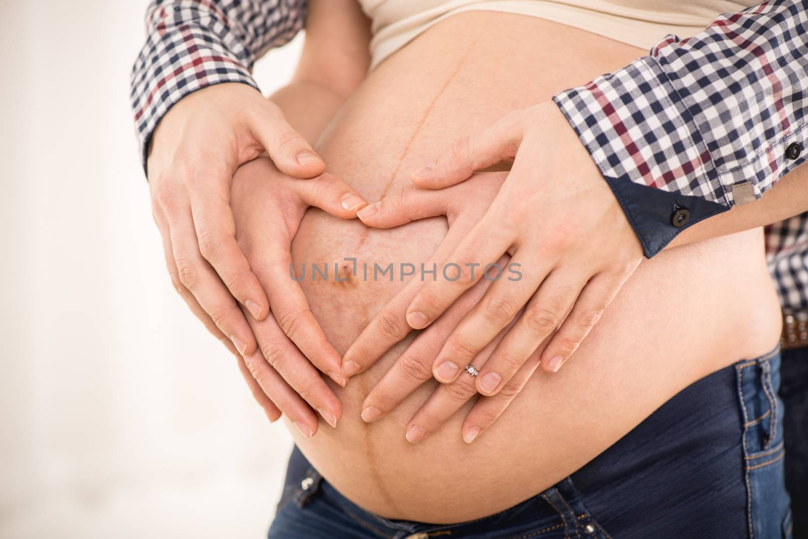 Male and female hands making a heart shape on the woman's pregnant belly. Close-up.