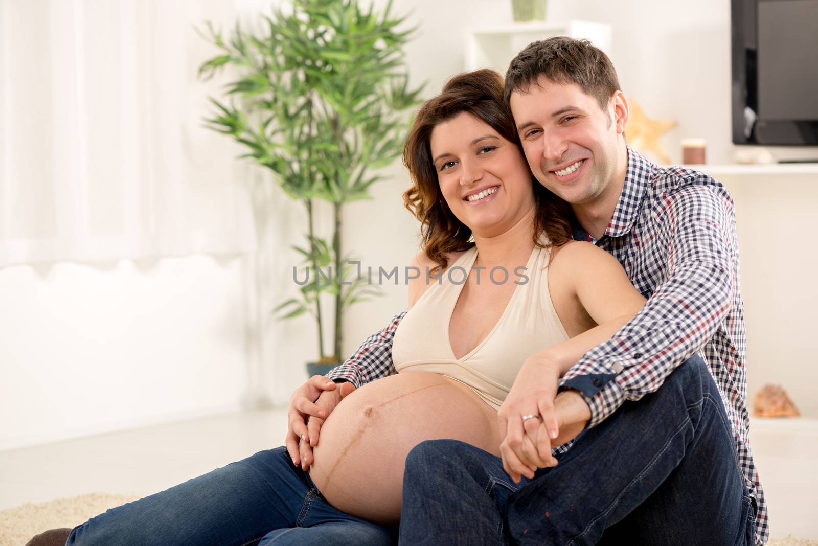Portrait of a beautiful young couple cuddling the woman's pregnant belly. They smiling and looking at camera.