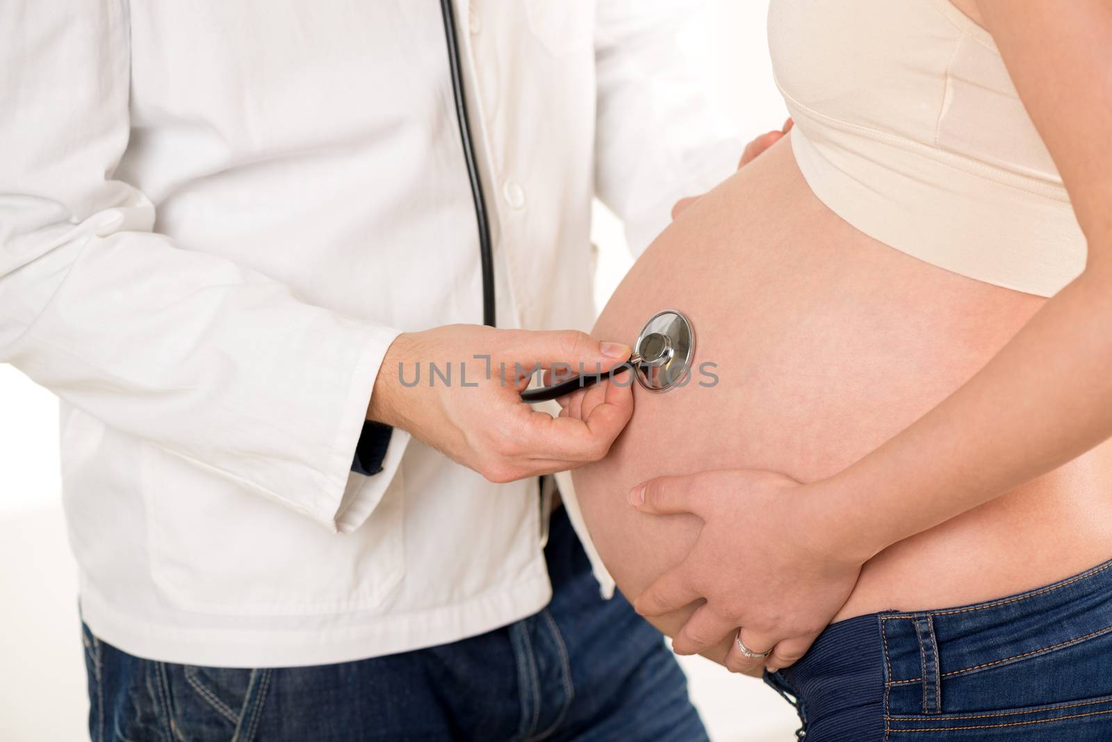 Pregnant woman examining by a doctor with a stethoscope. Close-up.