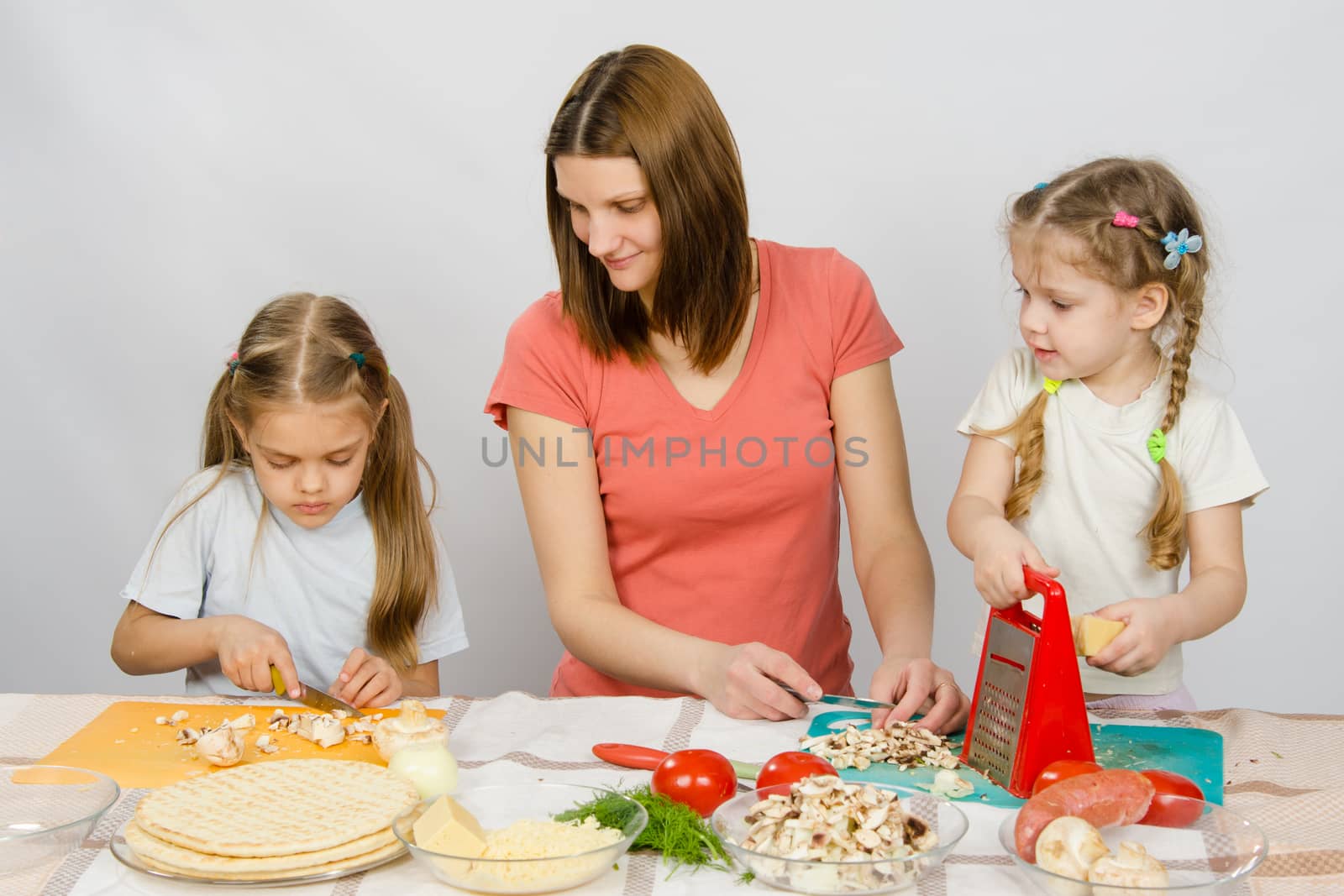 Mum with a five-year daughter watched as the eldest daughter cutting mushrooms pizza by Madhourse