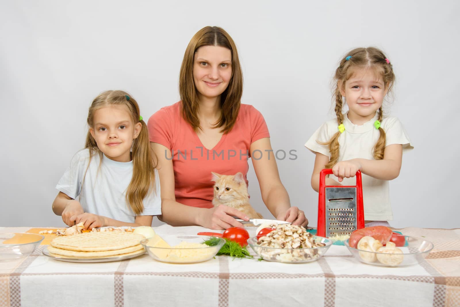 Mother and two little girls at a table prepared ingredients for the pizza. They were watching a cat