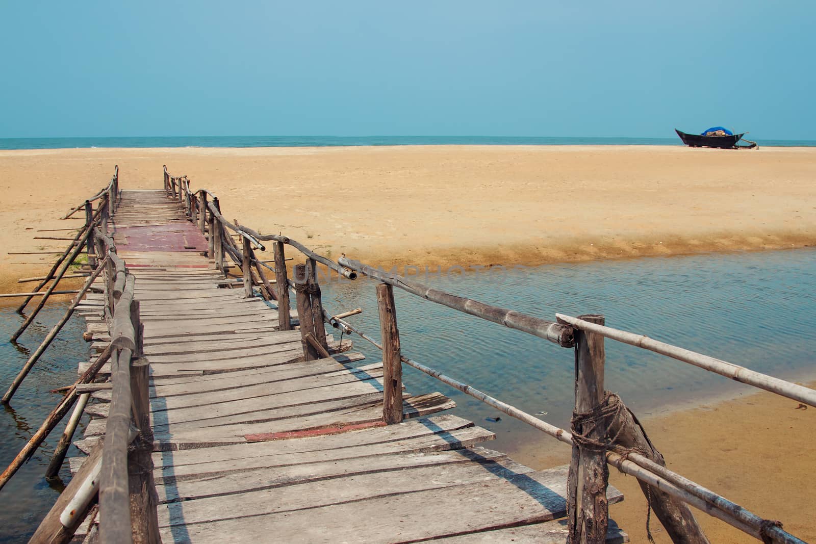 Creative travel photo with blue sky, sea, beach and wood plank road leading far away