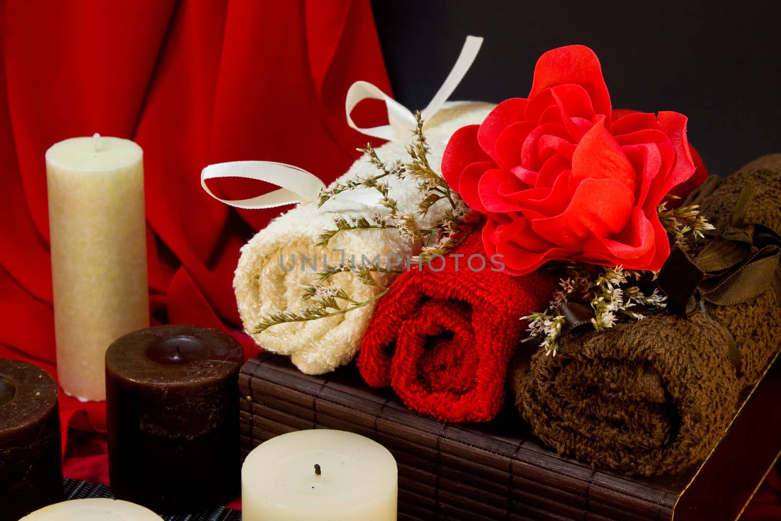 Spa still life of a candles, towels twisted into a roll, rose on a black and red background