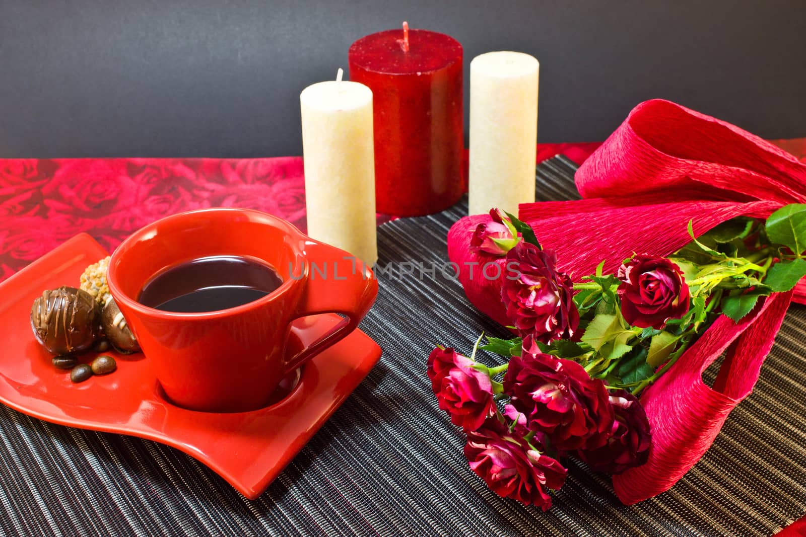 Coffee in red cup on a saucer with a chocolate and a bouquet of roses