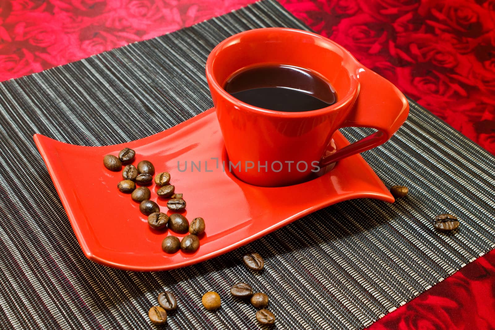 Coffee in red cup and saucer with coffee beans on a black napkin