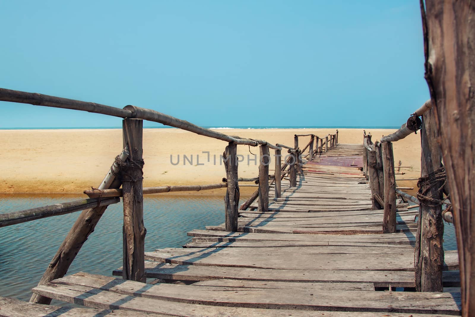 Creative travel photo with blue sky, sea, beach and wood plank road leading far away