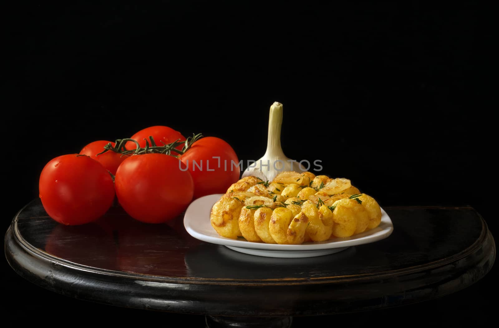 Roasted potatoes, garlic and tomatoes, black vintage table and black background.
