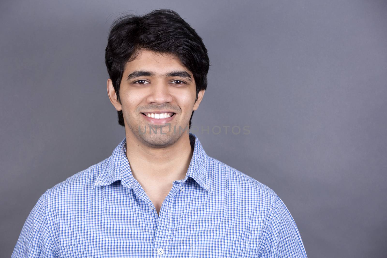 handsome east indian man wearing blue shirt on light grey background