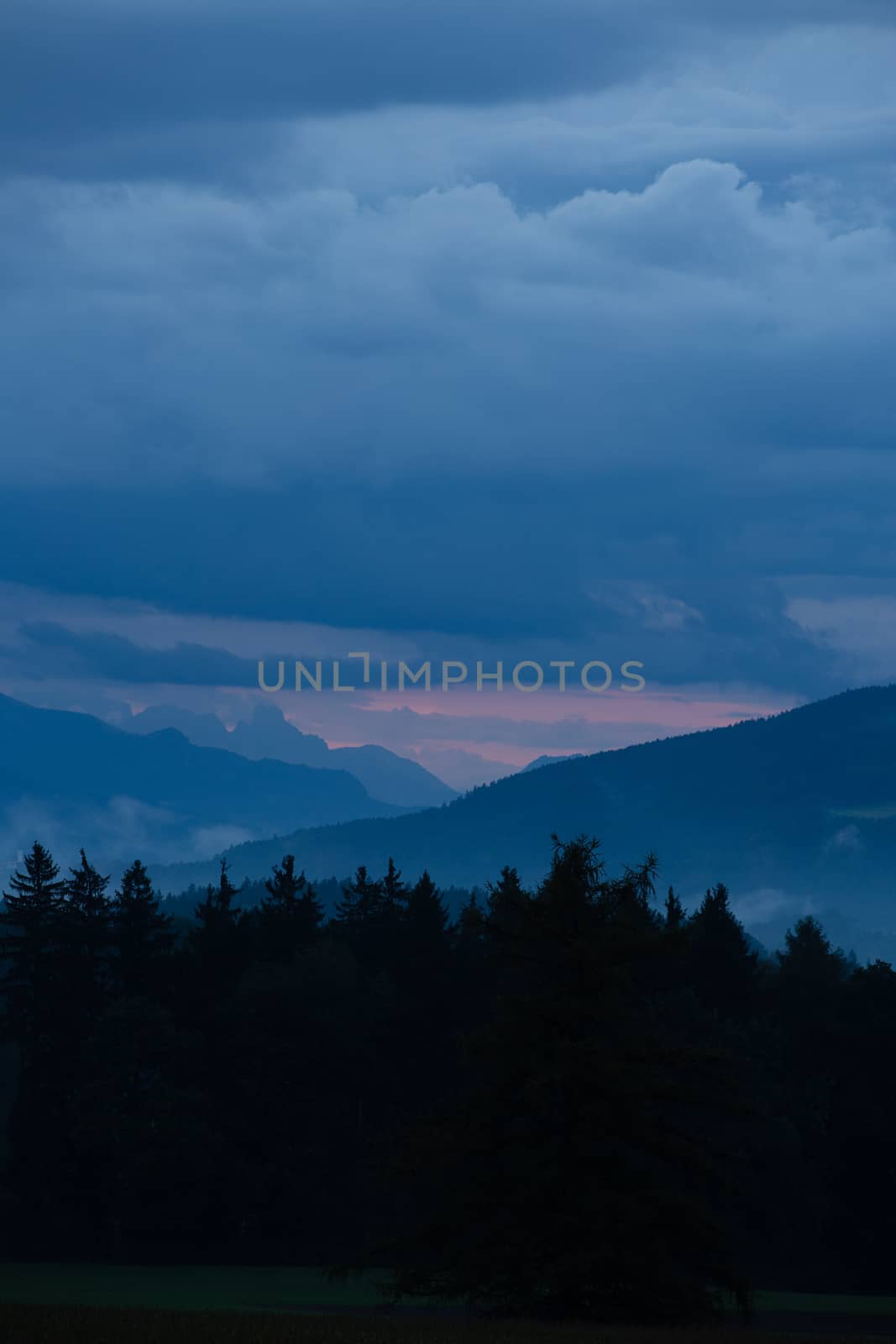 dark forest in front of mountain chain reddish shining horizon by maxlindna