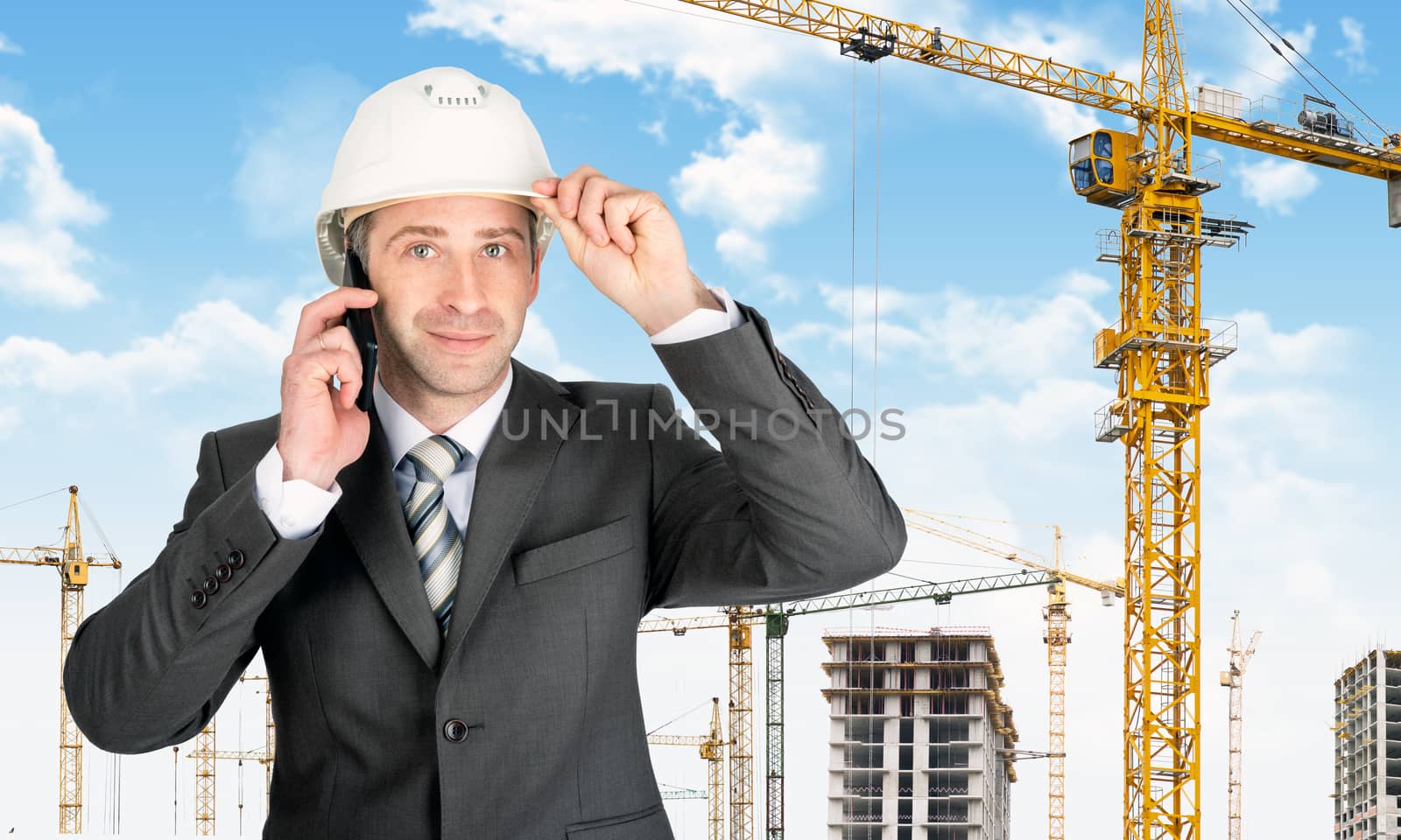Smiling businessman in helmet talking on mobile on building site