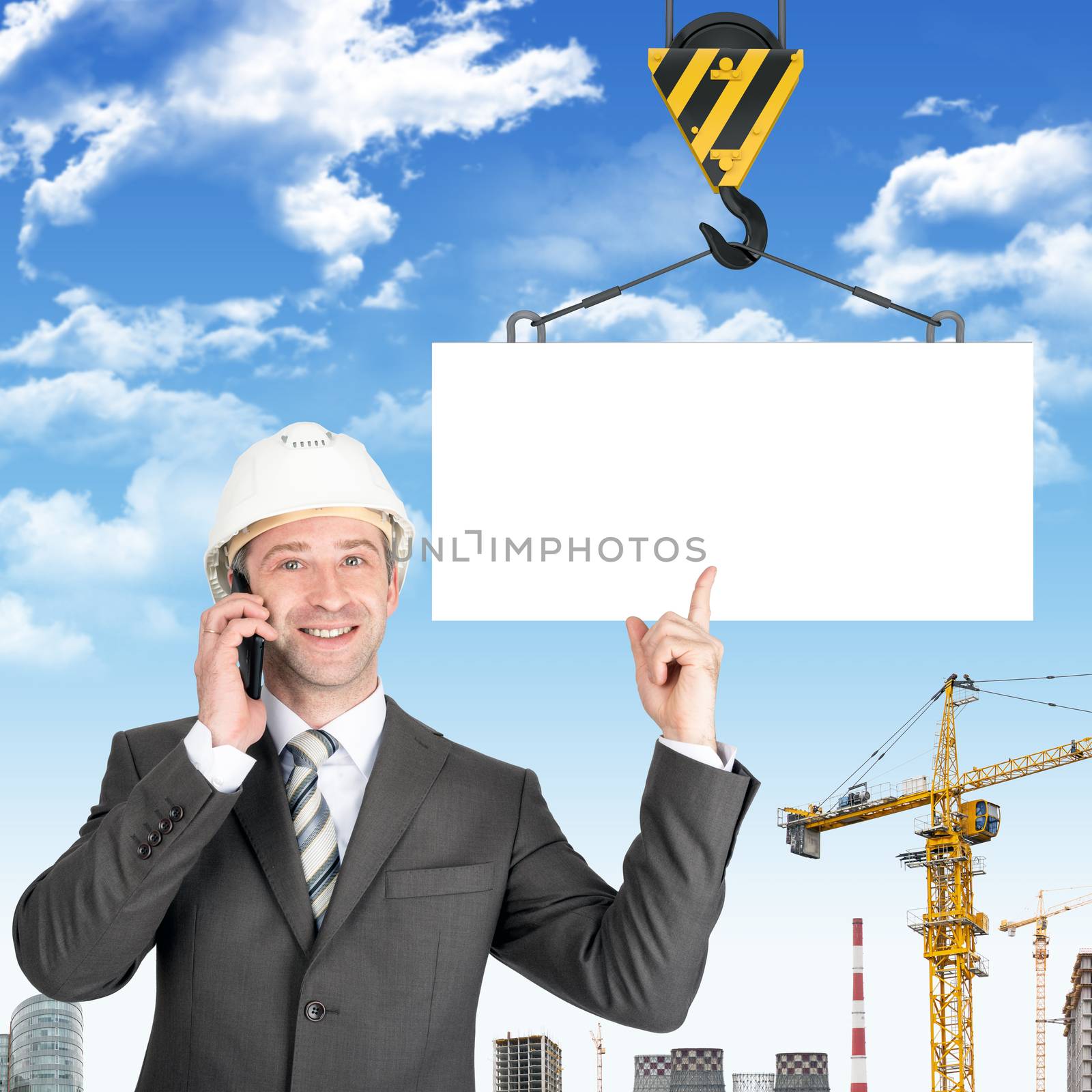 Smiling businessman in helmet talking on mobile with blank block on building site