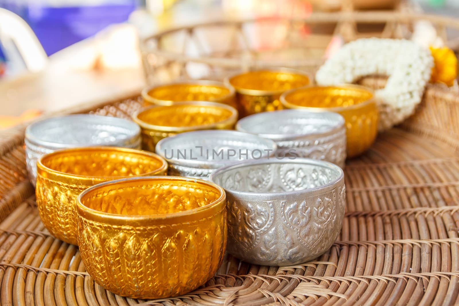 Gold and silver bowl on wooden basket and flower garland in background.