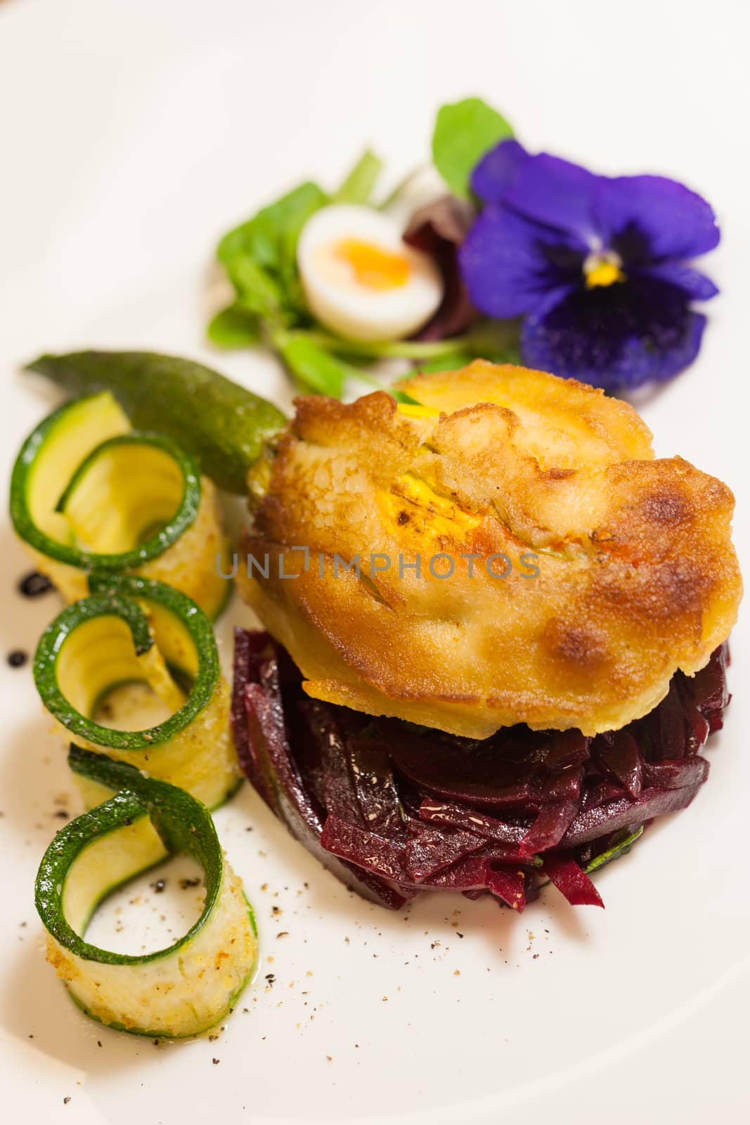 Delicious gourmet plate featuring biscuit sandwich with beets, zucchini strips and pansy garnish over white background