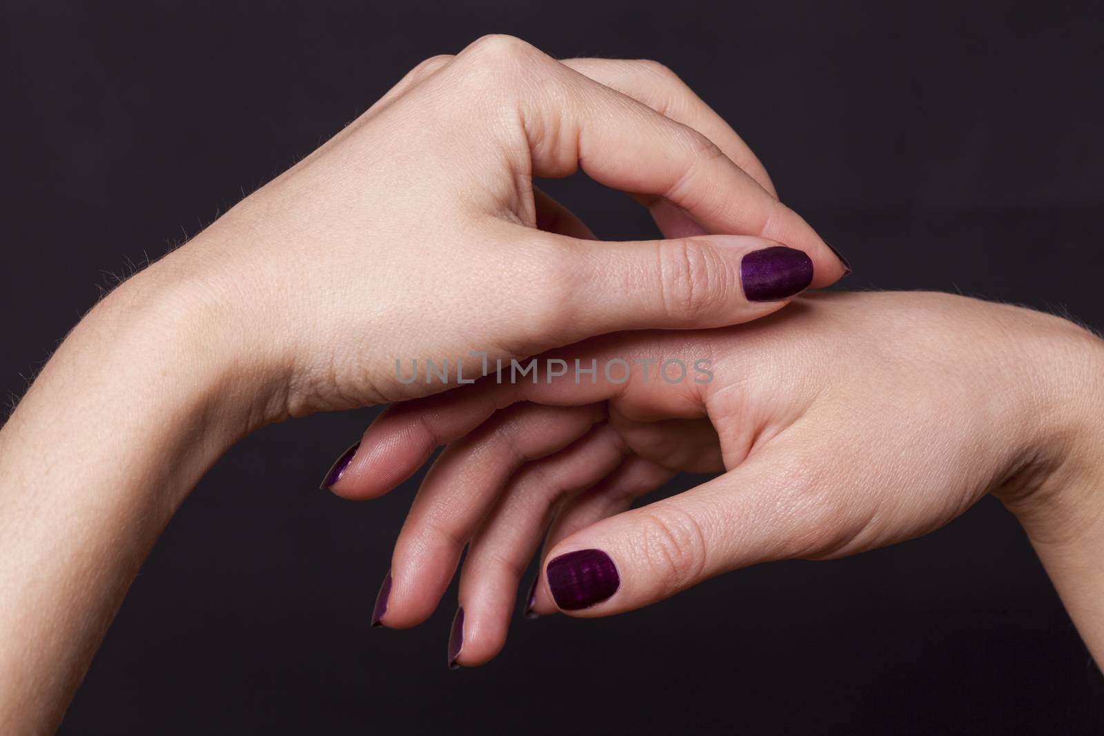 Close up of crossed over female hands decorated with purple fingernail paint over black