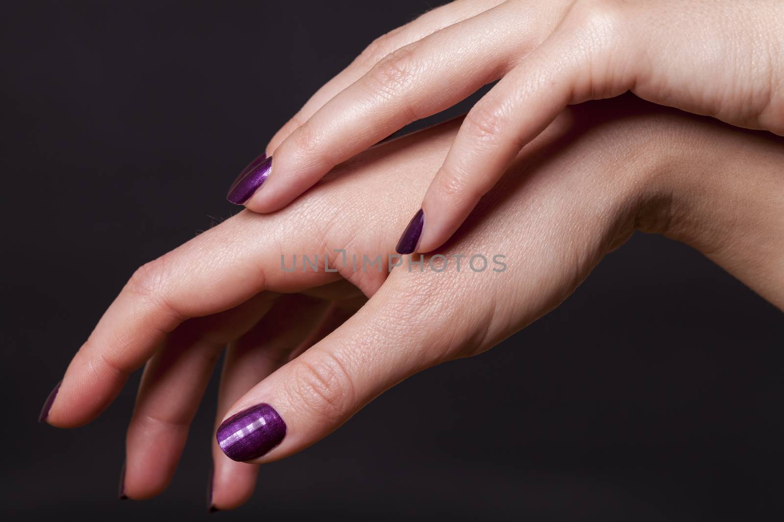 Close up of crossed over female hands decorated with purple fingernail paint over black