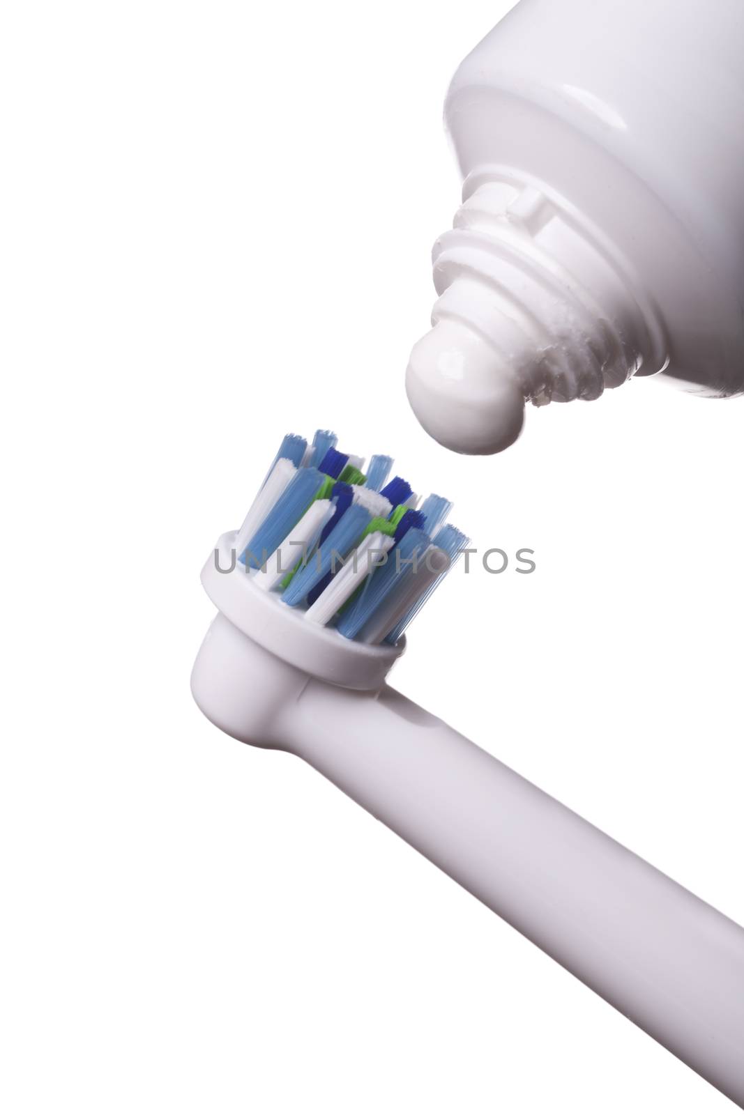 Close up of electric toothbrush with blue bristles and tube with paste bubbled at its opening on white background