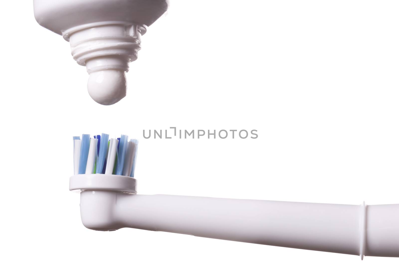 Close up of electric toothbrush with blue bristles and tube with paste bubbled at its opening on white background