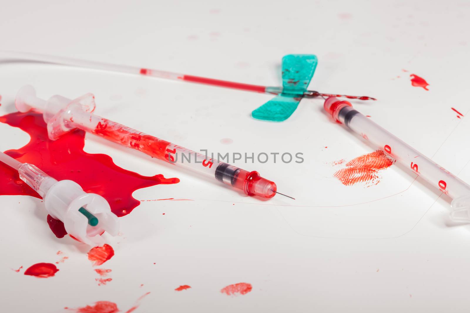 Concept Image - Surgical Aftermath Image of Needle Syringes and IV Lines Covered with Red Blood on White Background in Studio Still Life