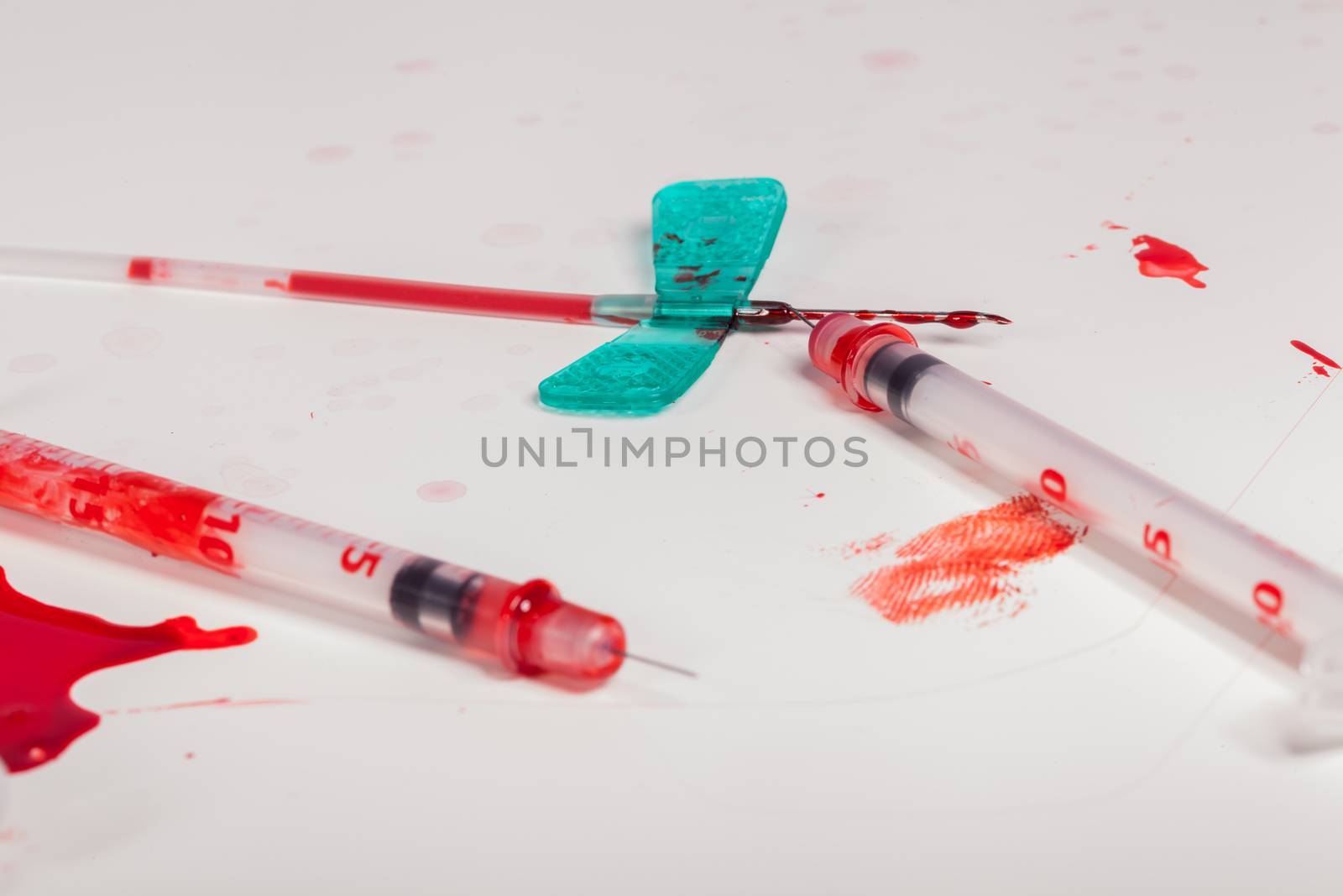 Concept Image - Surgical Aftermath Image of Needle Syringes and IV Lines Covered with Red Blood on White Background in Studio Still Life