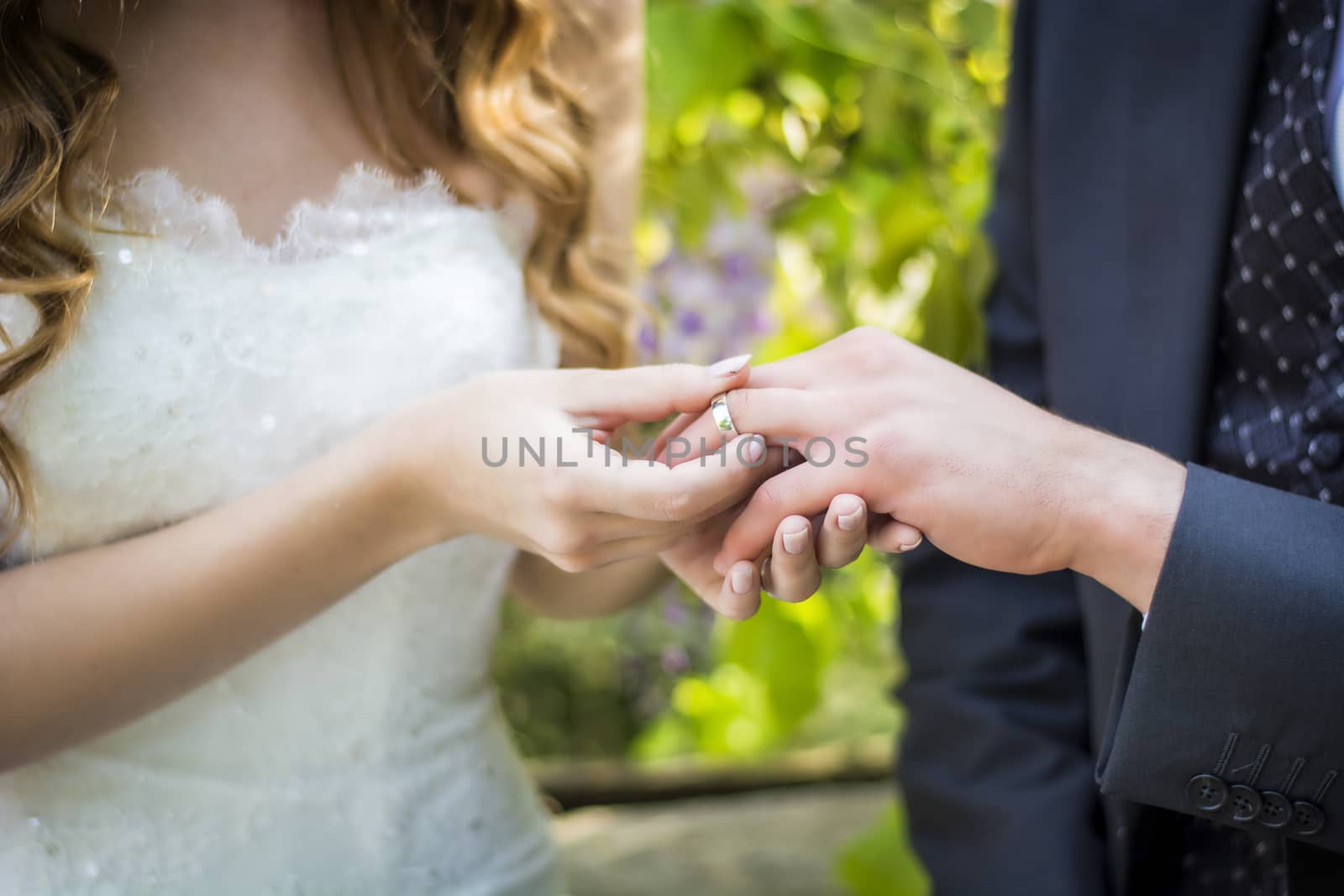 Close-up of bride putting wedding ring on groom's finger by artofphoto