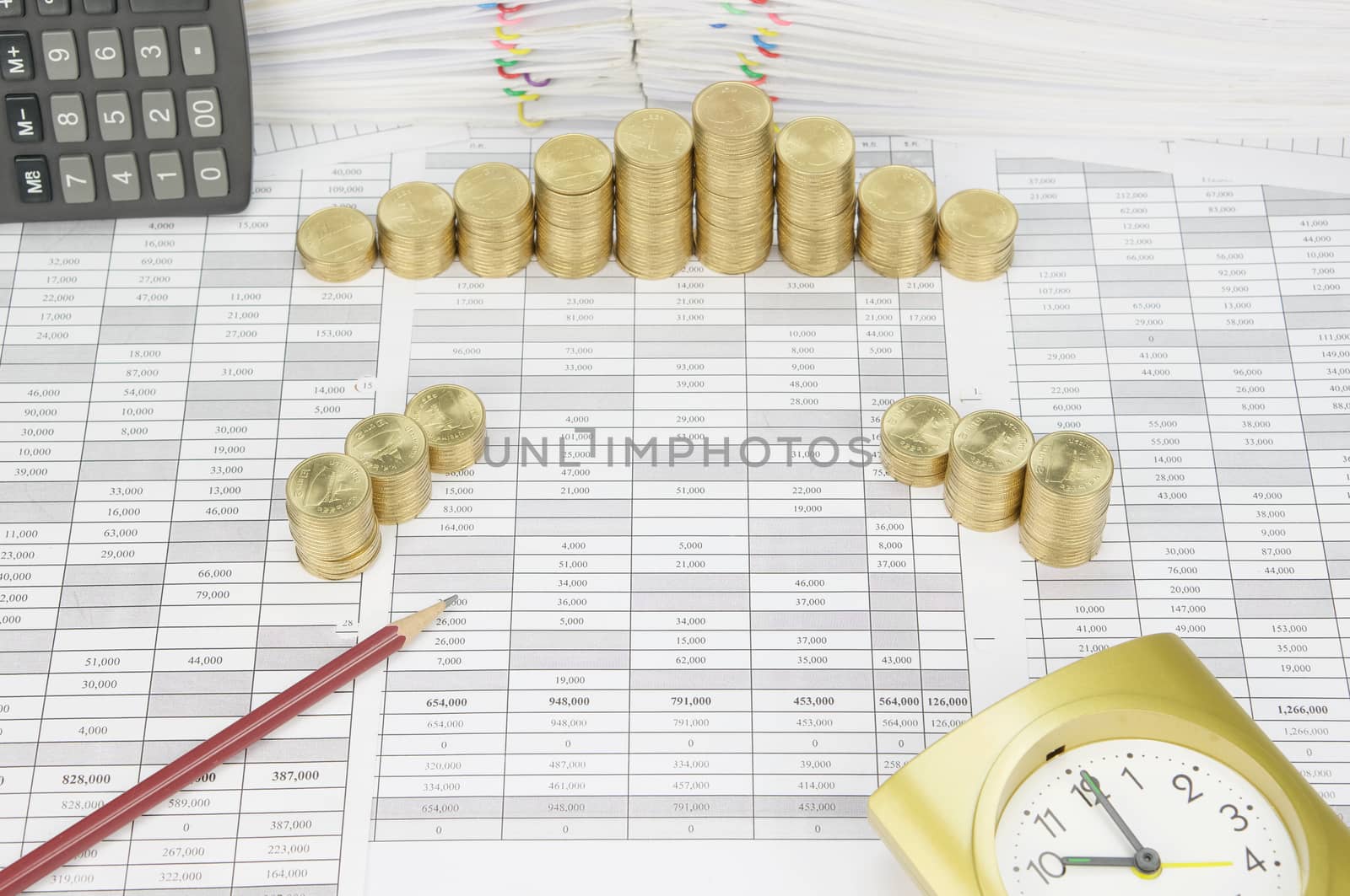 Brown pencil on finance account have step pile of gold coins with gold clock and pile of document as background.