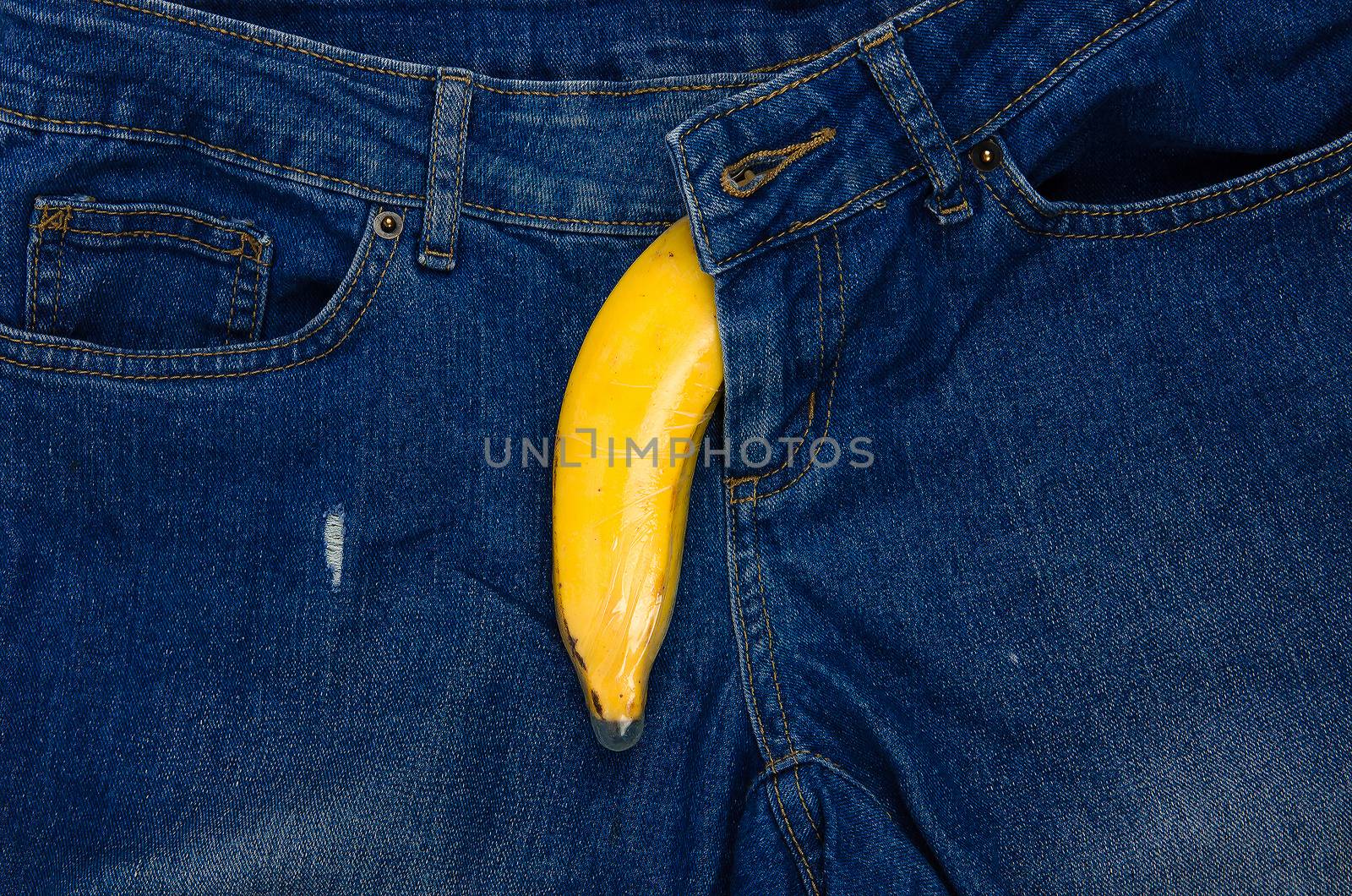 Condom and banana ready for safe sex on jeans background.