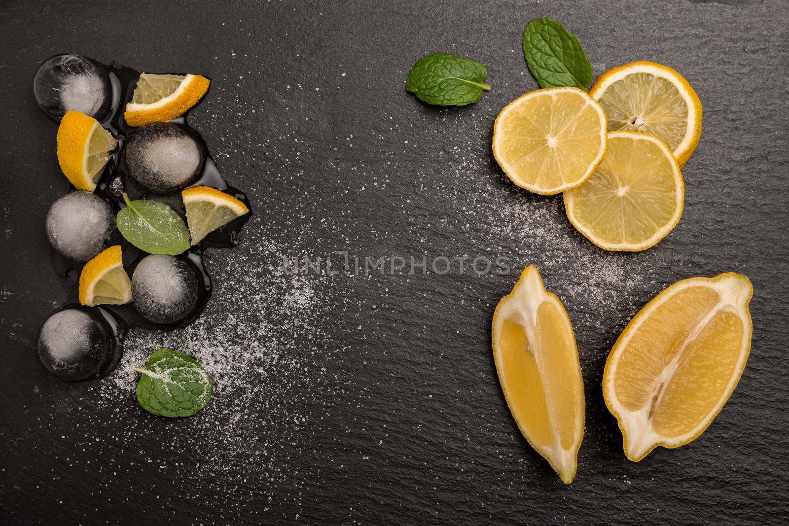 Slices and half fresh juicy lemon with mint leaves and melting ice on a slate board