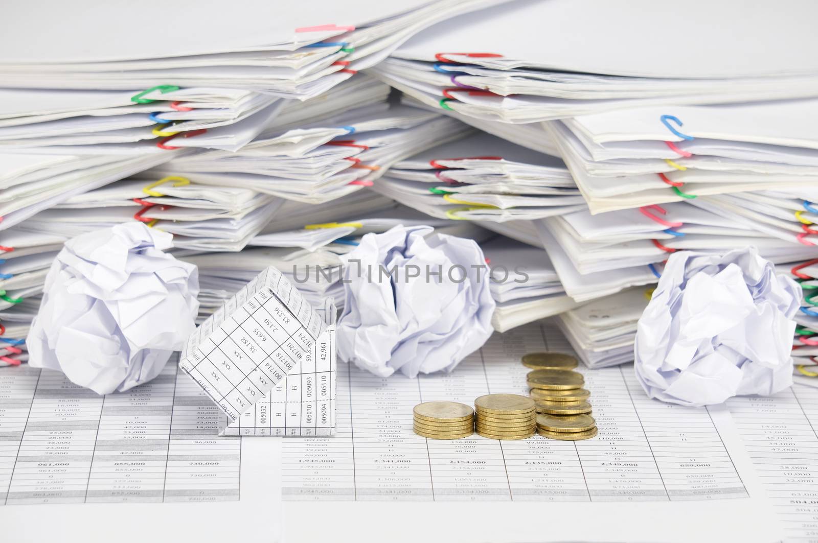 Bankruptcy of house with step pile of tumbledown gold coins on finance account have blur paper ball and pile of paperwork with colorful paperclip as background.