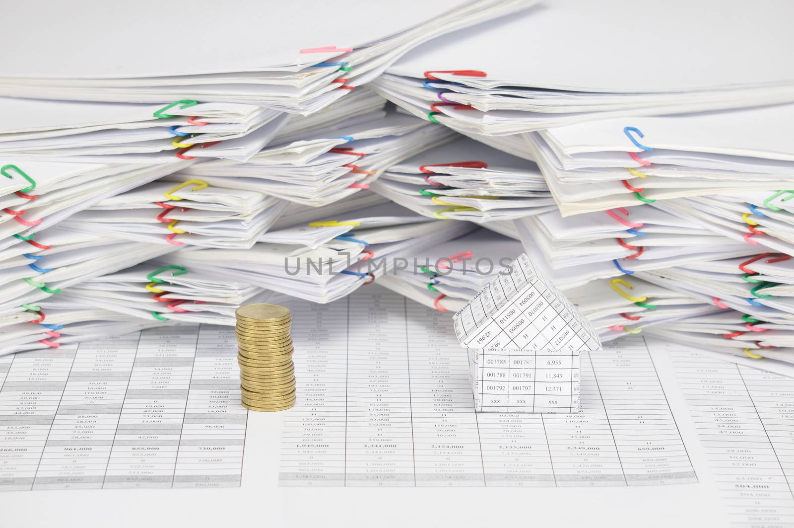 Pile of gold coins and house  on finance account have blur  overload of paperwork with colorful paperclip as background.