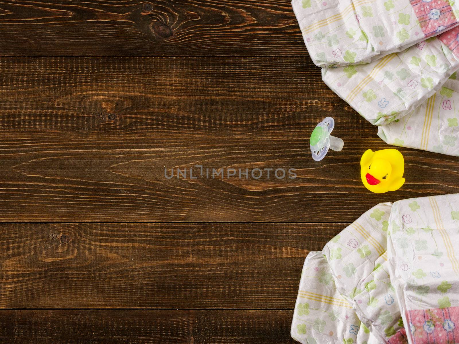 Japanese disposable diapers and dummy and rubber duckling on dark wooden background with copy-space. Flat lay
