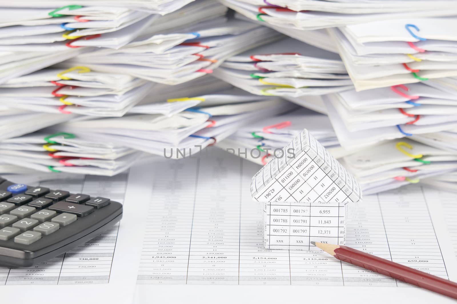 House with brown pencil and calculator on finance account have blur overload of paperwork with colorful paperclip as background.