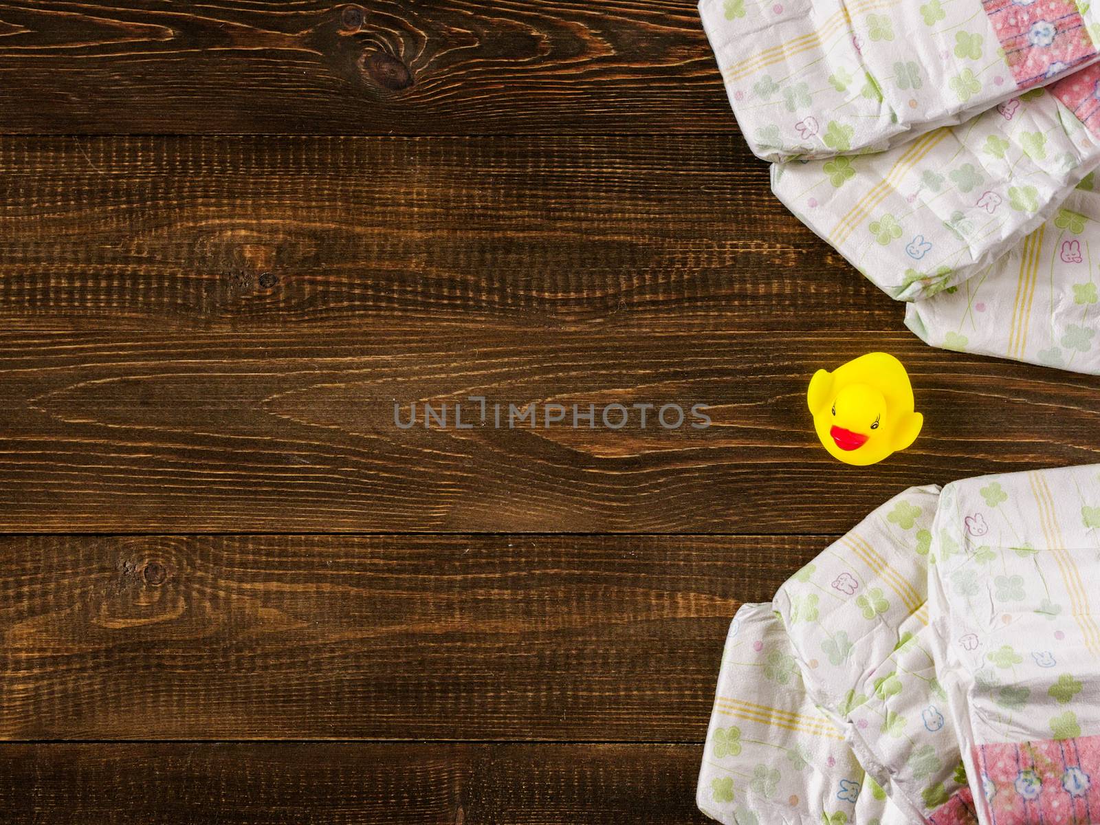 Japanese disposable diapers and the rubber duckling on dark wooden background with copy-space. Flat lay