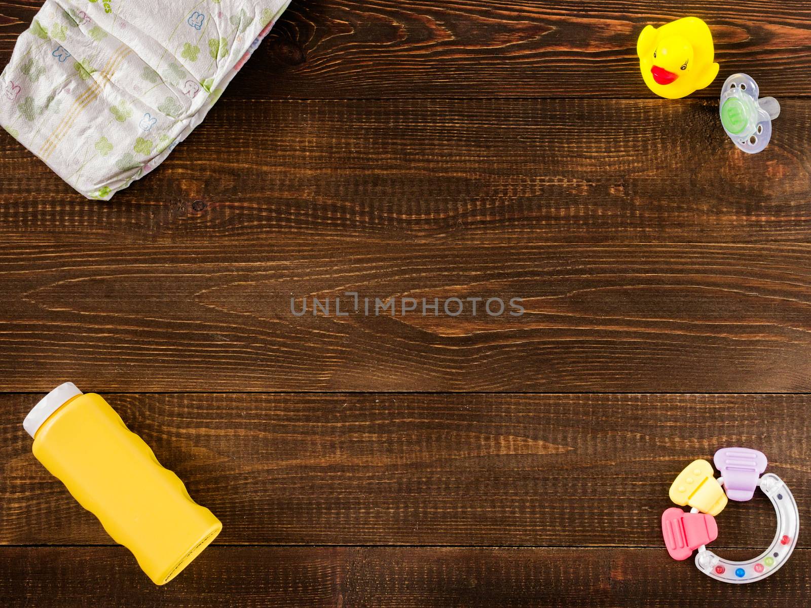 disposable diaper, teether, dummy, baby powder and rubber duckling on dark wooden background with copy-space. Flat lay
