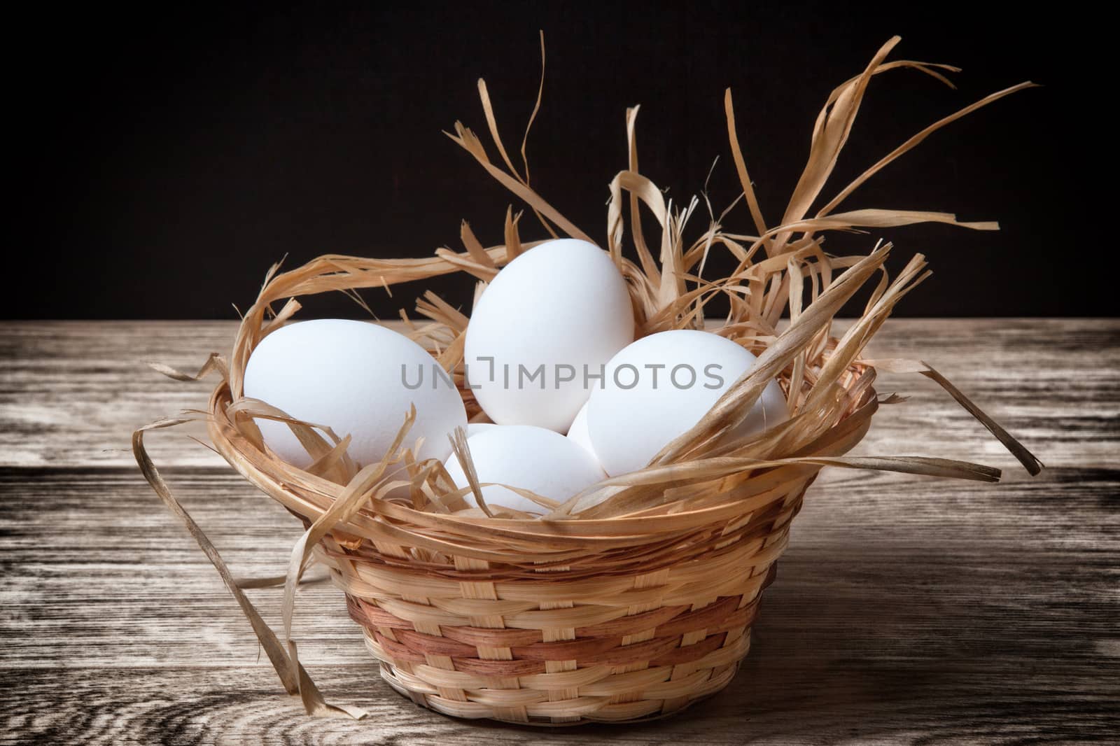 white chicken eggs in a wicker basket closeup on dark table