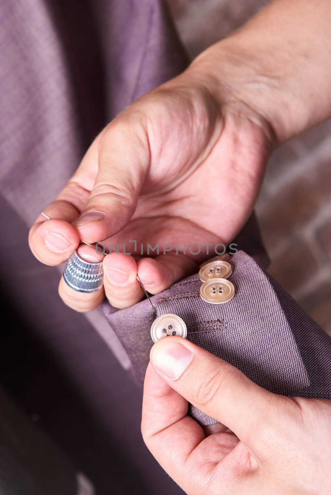 dressmaker sews a button on jacket by sarymsakov