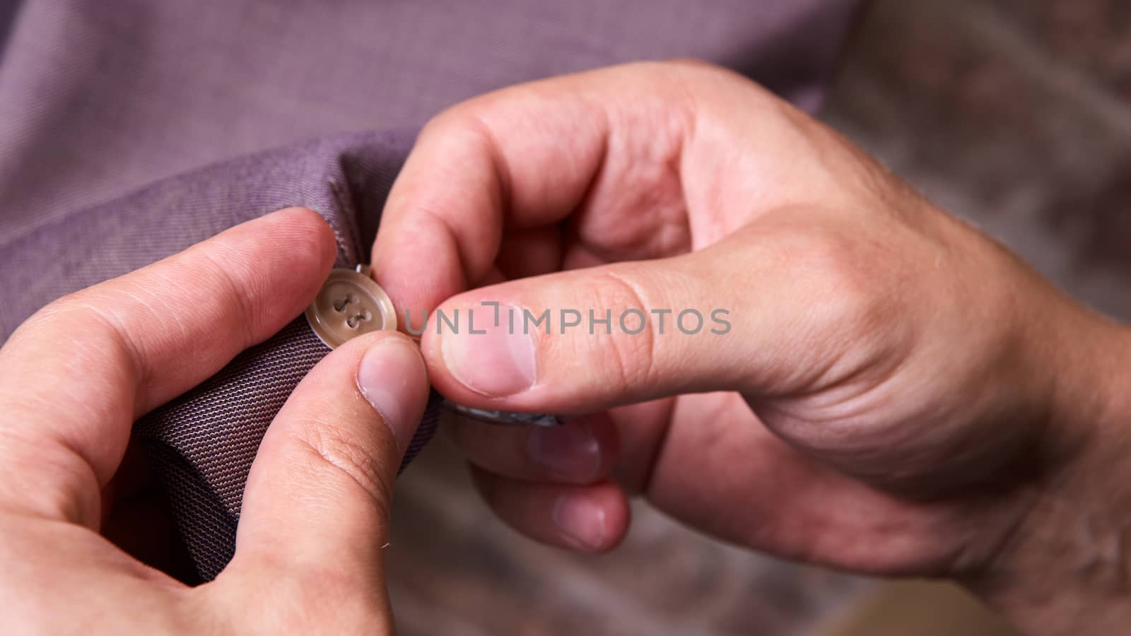 dressmaker sews a button on jacket by sarymsakov