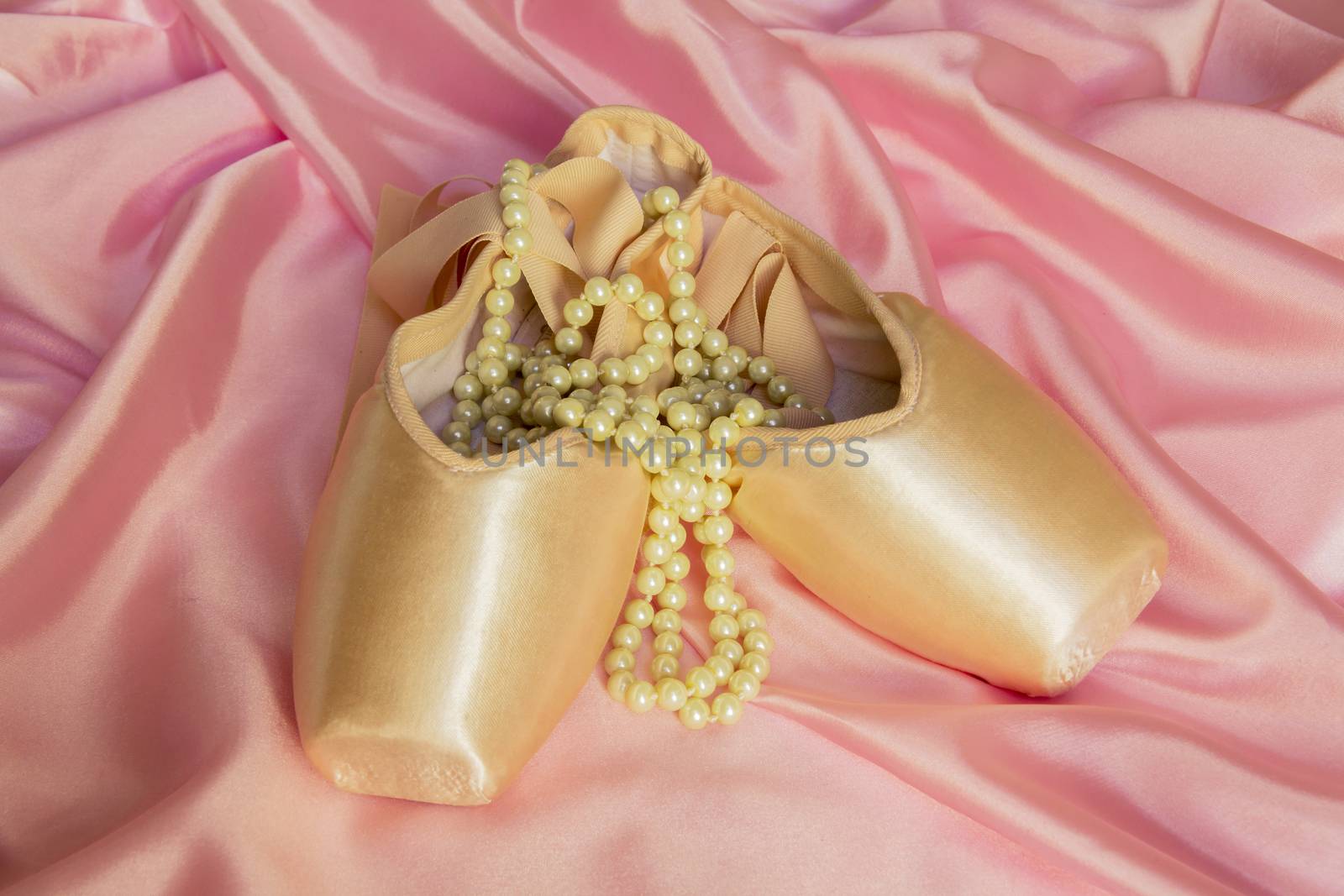 Ballet shoes and Pearl necklace on delicate pink silk background