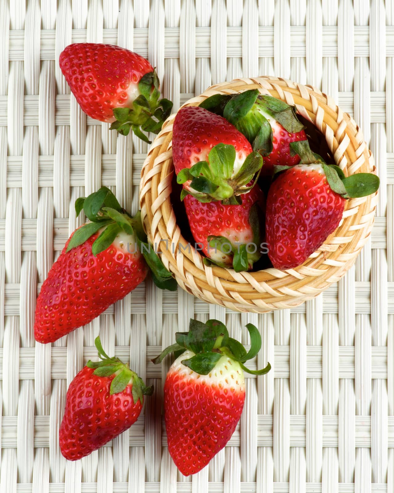 Arrangement of Fresh Ripe Strawberries in Wicker Bowl closeup on White Wicker background. Top View