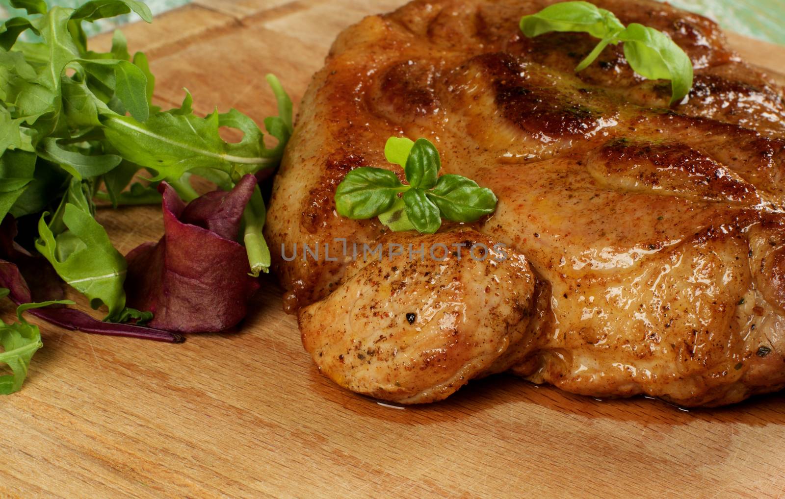 Delicious Juicy Roasted Pork Neck with Fresh Arugula, Mangold and Basil closeup on Wooden Cutting Board