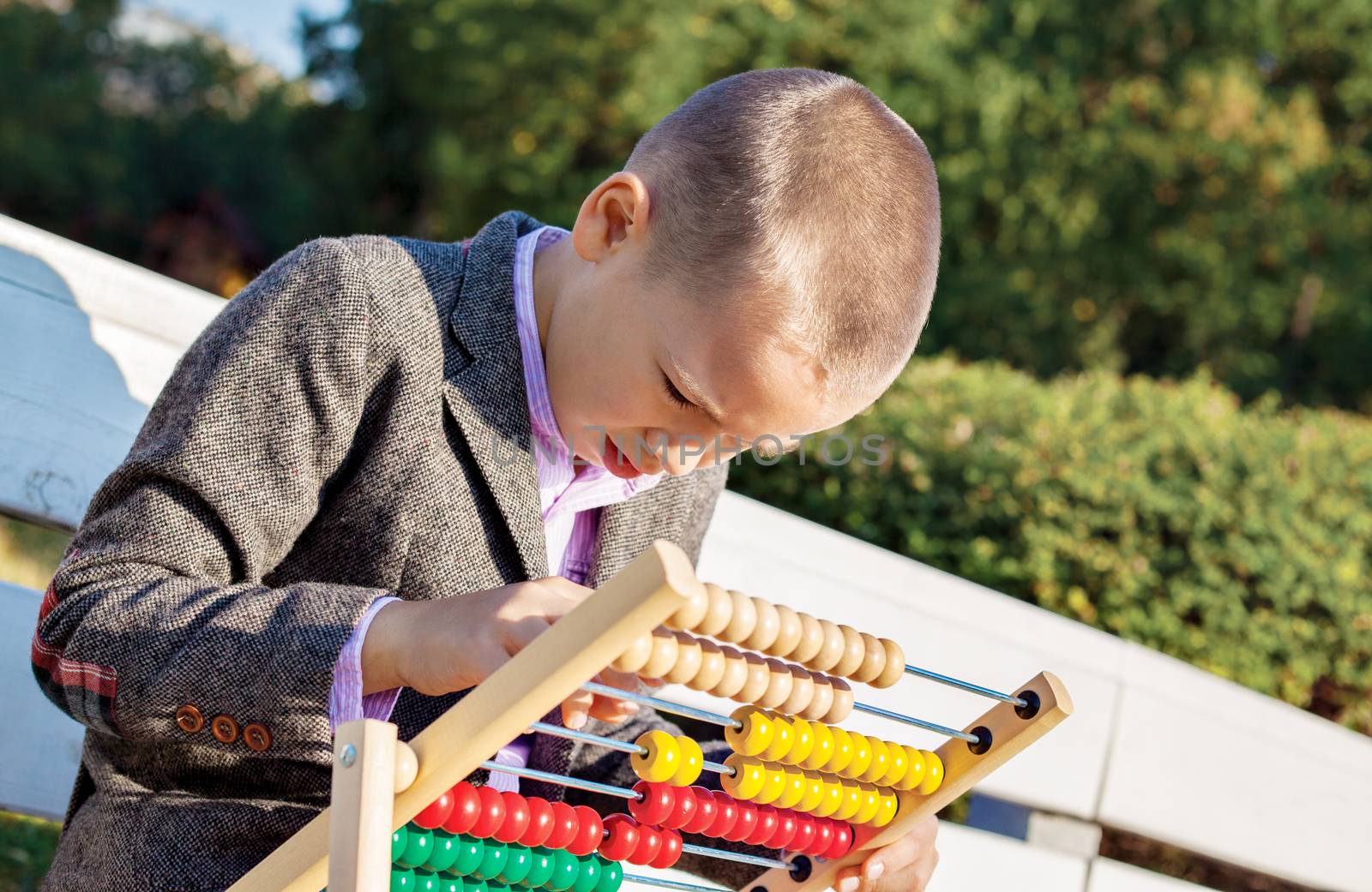 Back to school one little boy counting and playing on wooden abacus in the park.