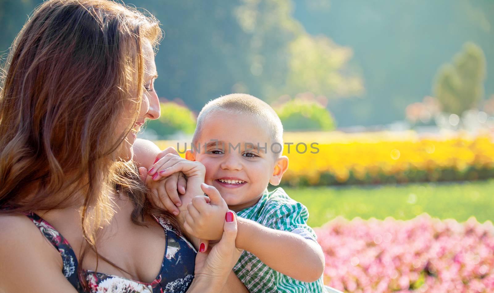 Happy little boy being embraced by his mother infront of a springtime blossom of a park.