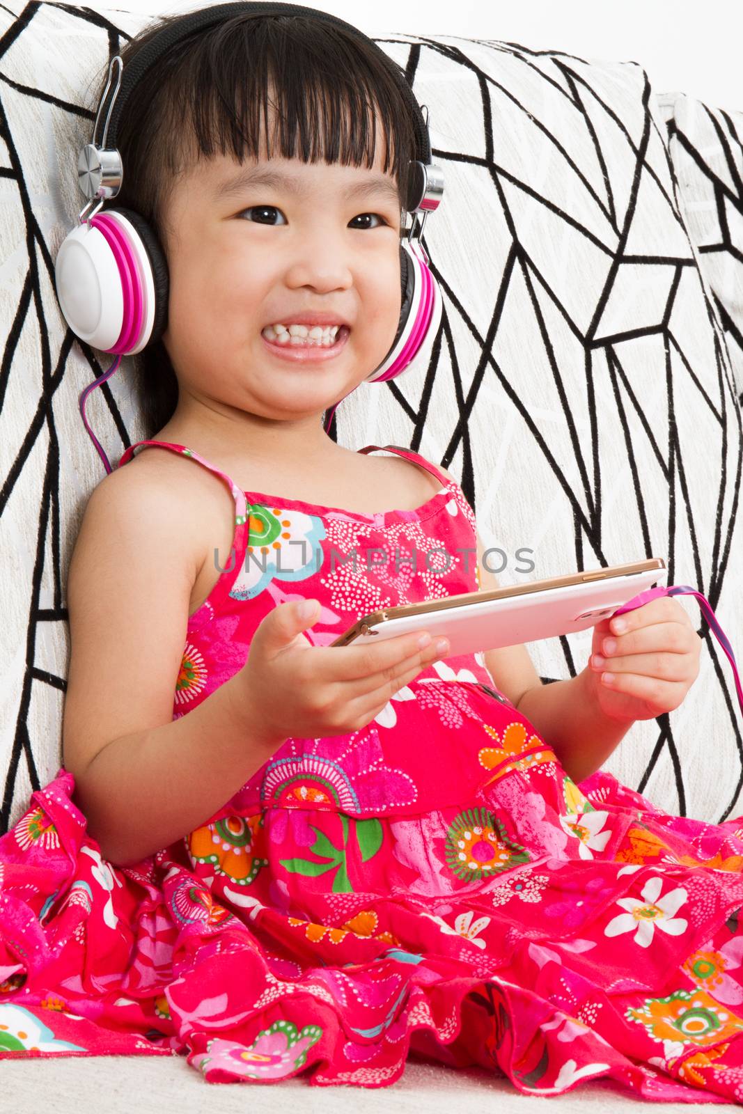 Chinese little girl on headphones holding mobile phone sitting on sofa